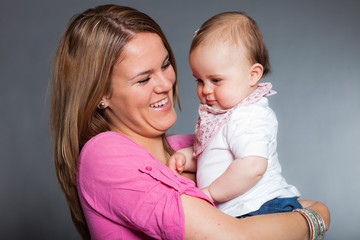 Happy young mother in love with her baby daughter. Studio shot.