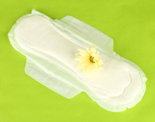 Panty liner and yellow flower on green background close-up