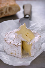 A whole cut camembert on waxed paper with rustic knife