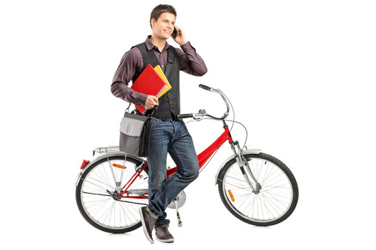 Smiling student holding books and talking on a phone next to a b