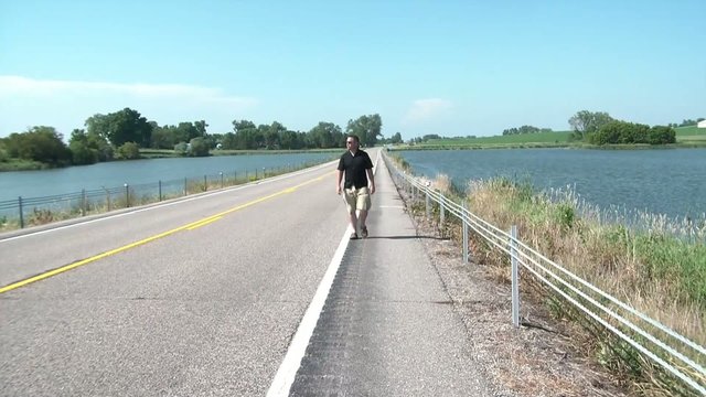Man Walks Down Road Between Lakes