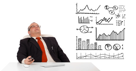 Businessman sitting at desk with diagrams and holding a mobileph