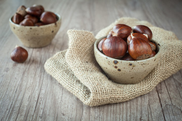 Fototapeta premium Bunch of fresh chestnuts in a bowl on wooden table