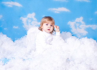 Baby with angel wings sitting in the clouds