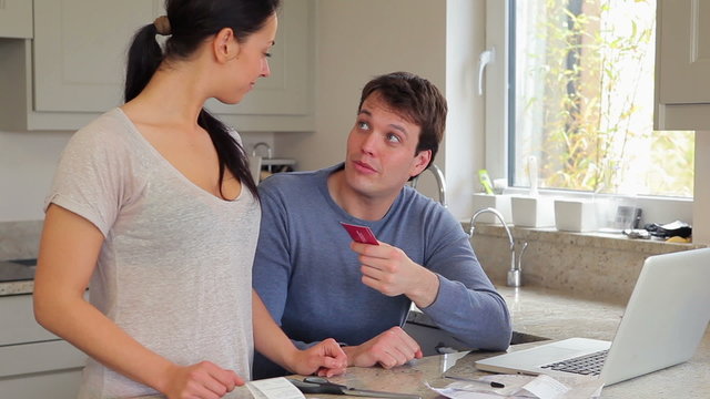 Couple discussing finances at laptop and cutting credit card