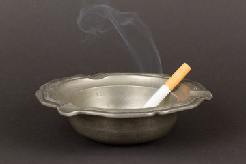 Burning cigarette in an old tin ashtray