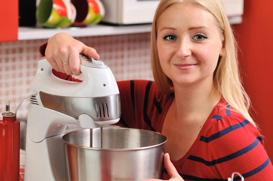 Young Blonde Woman Using A Mixer In Red Kitchen.