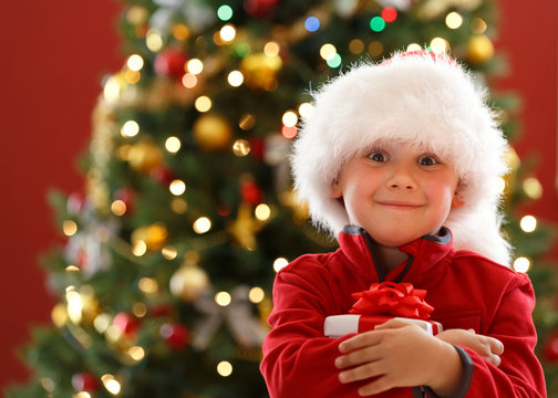Little boy holding Christmas gift box, decorated Christmas tree on background