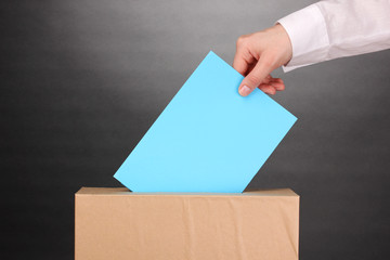 Hand with voting ballot and box on grey background