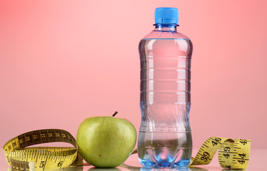 Bottle of water, apple and measuring tape on pink background