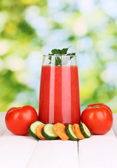 Glass of tomato juice on wooden table, on green background