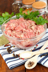 Bowl of raw ground meat with spices on wooden table