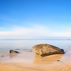 Flat rock on a golden sand beach and sea. Long exposure.