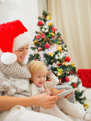 Obraz na płótnie Canvas Happy mother and kid using tablet PC near Christmas tree