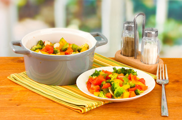 Vegetable stew in gray pot on wooden table on bright background