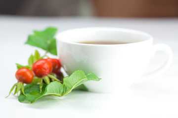 cup of tea and rosehip berries with leaves on white background