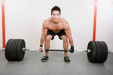 Fototapeta premium Young and muscular guy holding a barbell. Crossfit dead lift ex