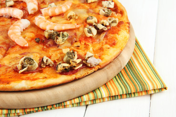Delicious pizza with seafood on stand on wooden background