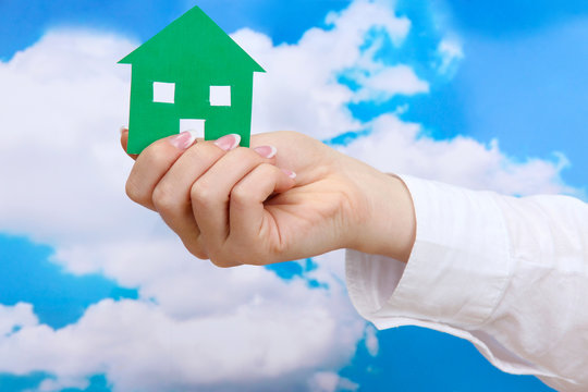 concept: woman hand with paper house on sky background, close