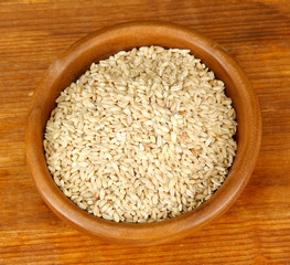 Raw buckwheat in wooden bowl on table on brown background