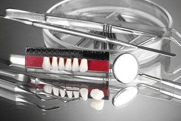 Set of dental tools with denture on grey background