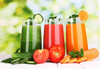 Fresh vegetable juices on wooden table, on green background