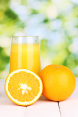 Glass of fresh orange juice on wooden table, on green