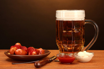 Beer and grilled sausages on wooden table on brown background