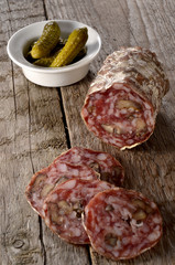 A walnut salami on a wooden board with cornichons