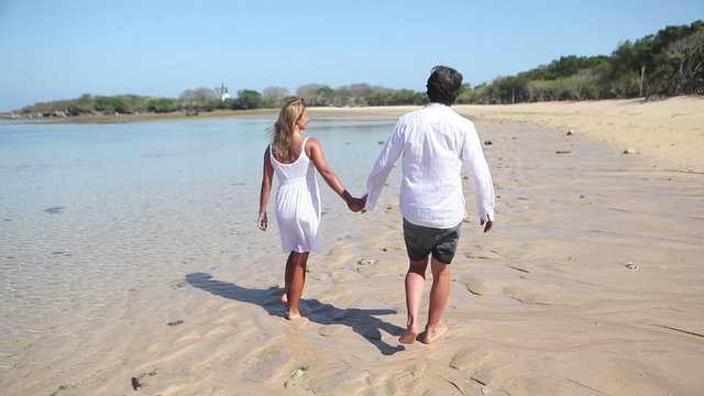 couple holding by hands and walking along coastline