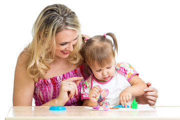 Naklejka premium Happy little kid and mother sitting at table and playing with co