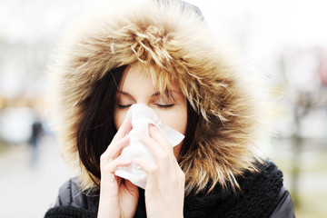 Woman sneezes during cold day and holds a tissue.