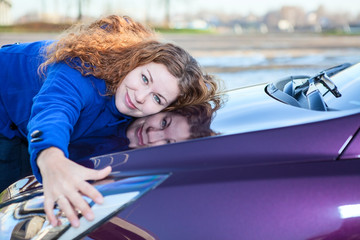 Young female driver embracing hood of new car