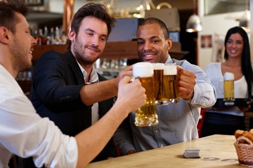 Friends clinking with beer mugs in pub