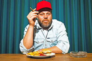 Man with beard and eating fast food meal and smoking cigar.