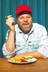 Man with beard and eating fast food meal and smoking cigar.