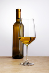 bottle of white wine with glass flat on the table with a white b