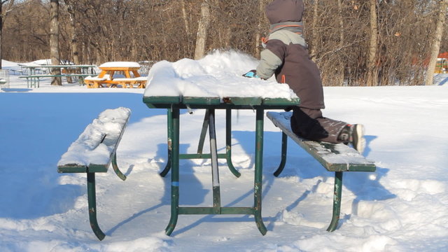 Boy removes snow from a table in the park in winter.