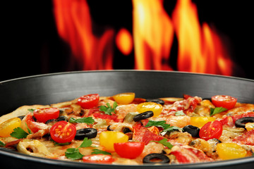 Delicious pizza with seafood on fire background