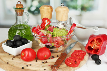Fresh greek salad in glass bowl surrounded by ingredients for