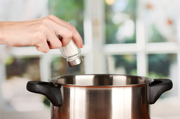 Hand adding salt using  salt shaker on bright background
