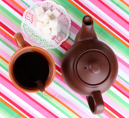 Top view of cup of tea and teapot on colorful tablecloths