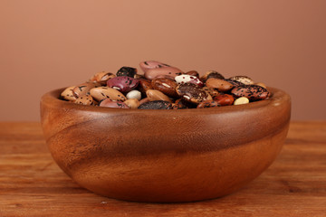 Wooden bowl with beans on wooden table on brown background