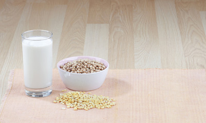 A glass of soy milk with a bowl of raw soybean and  seed