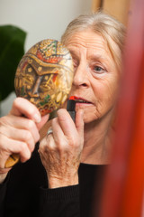 Fototapeta premium Good looking senior woman doing make-up in front of mirror.