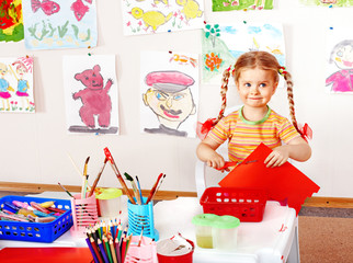 Child with scissors cut  paper  in playroom.