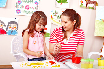 Child with teacher draw paints in play room.