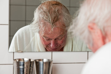 Senior man in front of mirror in bathroom.