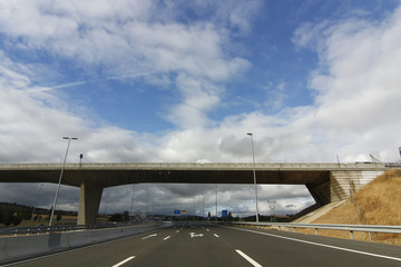 Fototapeta na wymiar highway with bridge crossing the road and blue sky with white cl
