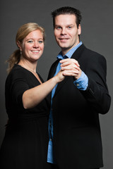Stylish happy young couple dancing. Studio shot against grey.